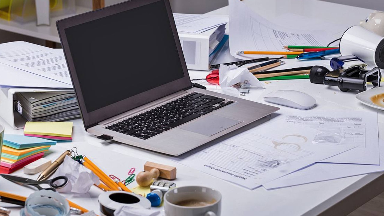 a cluttered workspace, with a laptop and many papers laying about.